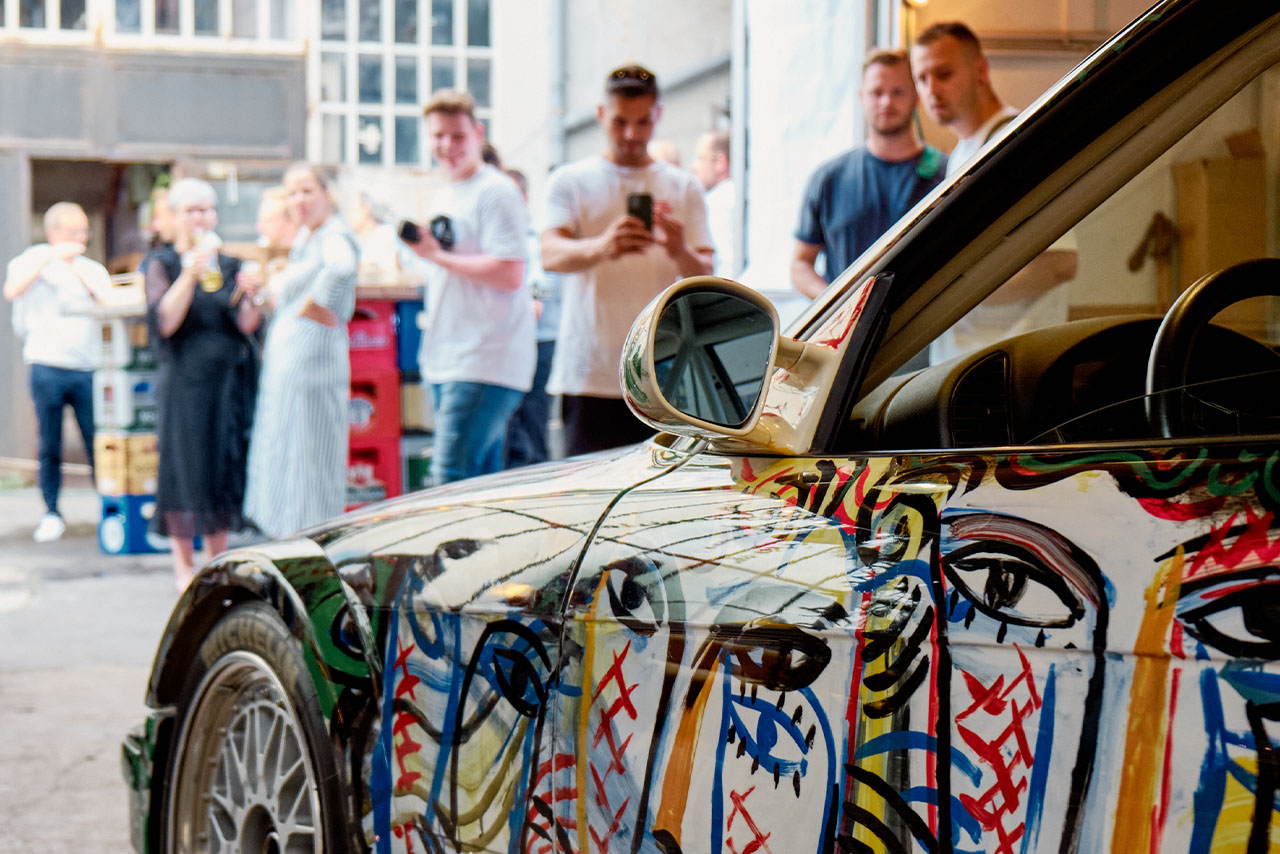 A colorful BMW Classic car is parked in front of a group of people on the street.