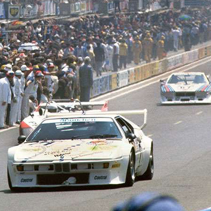 BMW M1 racing car during the race at the 24 Hours of Le Mans, surrounded by other vehicles on the track.